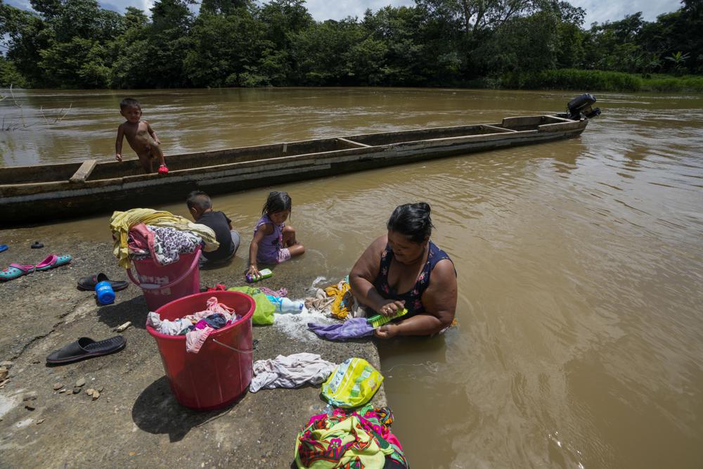 Mariela Lino lava ropa acompañada de sus nietos en la ribera del río Chucunaque, en Peñitas, provincia de Darién, Panamá, el viernes 1 de octubre de 2021. Peñitas sirvió hasta hace poco como uno de los lugares de recepción para la migración irregular en la zona. (Foto AP/Arnulfo Franco)