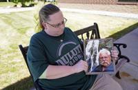 Ann Haas poses June 18, 2021, in Eden Prairie, Minn., with a photo she took of her late father, Raymond Haas. Haas lost her father to COVID-19 on Nov. 11 and works in the laundry at the same Veterans Affairs hospital where he spent his final days. Haas said memories coming flooding back each time she folds a tan blanket like the one that covered him while he was fighting to live. (AP Photo/Jim Mone)