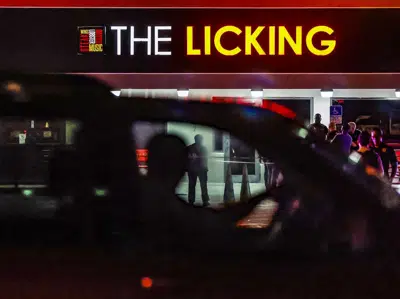 Varios transeúntes observan cómo los policías de Miami Gardens trabajan en los alrededores del restaurante The Licking después de que, según versiones, varias personas resultaran heridas a disparos la noche del jueves 5 de enero de 2023 en Miami Gardens, Florida. (Al Díaz/Miami Herald vía AP)