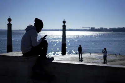 Un adolescente revisa su celular frente al Río Tagus, en Lisboa, Portugal, el lunes 30 de enero de 2023. (AP Foto/Armando Franca)