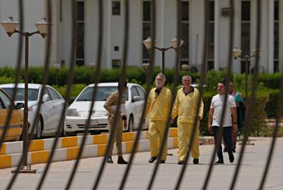 Jim Fitton (en el centro, a la izquierda) y Volker Waldmann (en el centro, a la derecha) caminan esposados frente a un edificio de tribunales en Bagdad, Irak, el domingo 15 de mayo de 2022. Fitton, de Gran Bretaña, y Waldmann, de Alemania, son acusados de sacar antigüedades de Irak de contrabando. (AP Foto/Hadi Mizban)