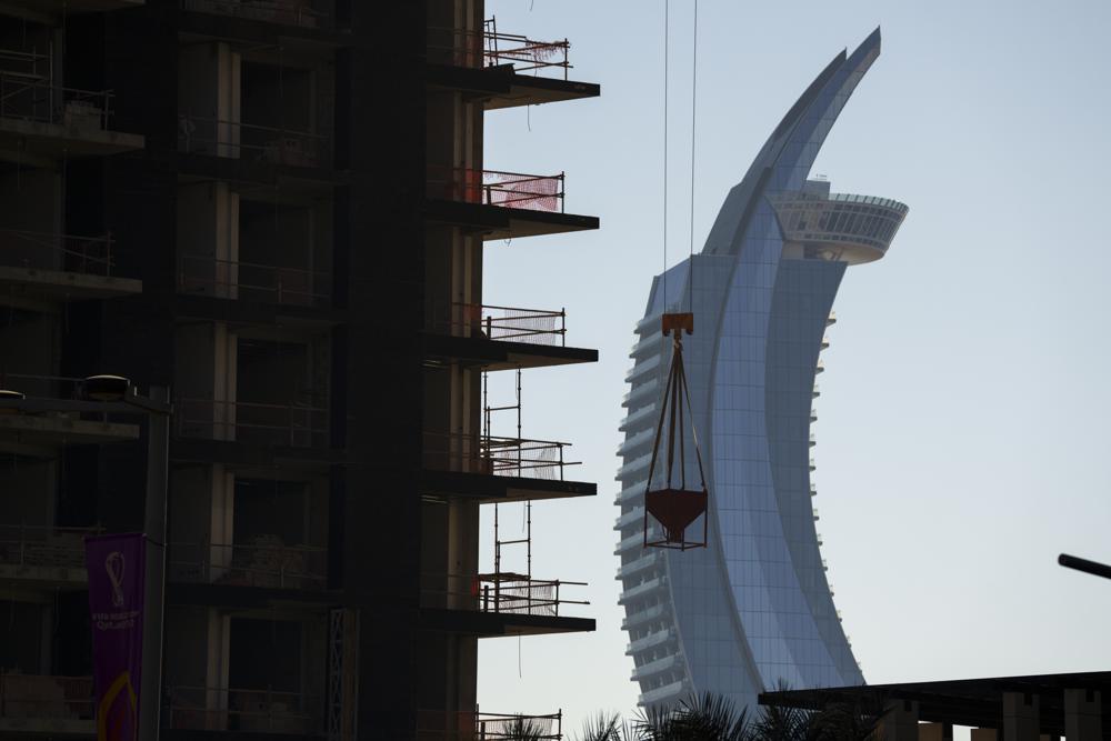 Una grúa trabaja en un edificio en construicción, con las torres con forma de media luna de Lusail en segundo plano, en el centro de Lusail, Qatar, el 24 de noviembre de 2022. (AP Foto/Pavel Golovkin)