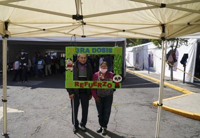 ARCHIVO - Una pareja posa para una foto sosteniendo un marco con un mensaje que dice: "Tercera dosis, vacúnese, refuerzo", luego de recibir un refuerzo de AstraZeneca contra el COVID-19 durante una campaña de vacunación para personas de 60 años y más, en Ciudad de México el 4 de enero de 2022. (AP Foto/Fernando Llano, Archivo)