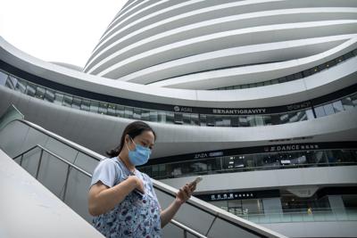 Una mujer con una mascarilla para protegerse del coronavirus camina en un complejo de tiendas y oficinas el martes 27 de julio de 2021, en Beijing. (AP Foto/Mark Schiefelbein)
