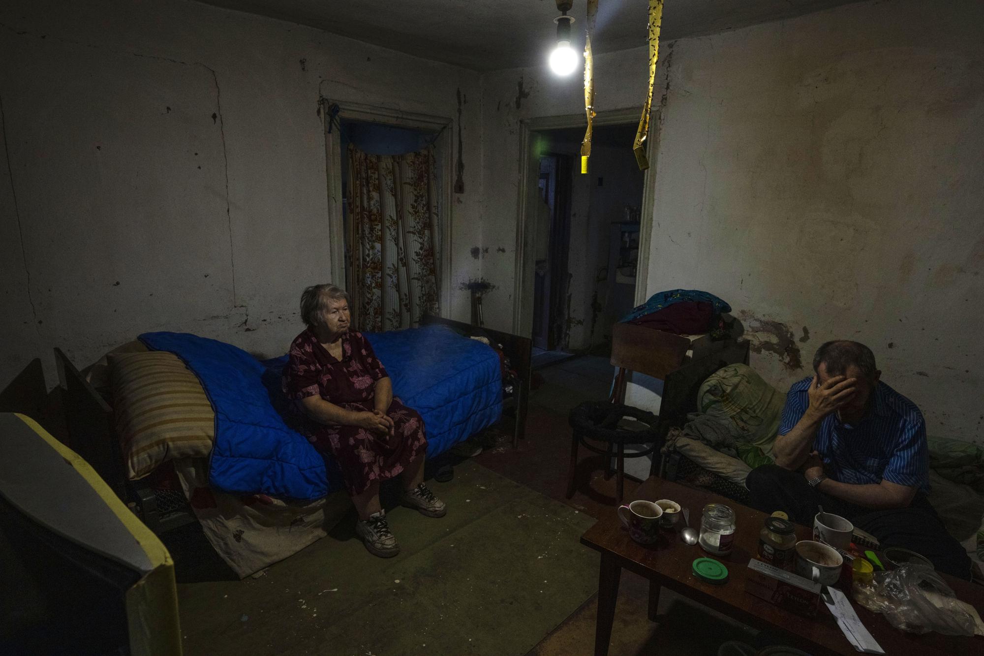 Tamara Markova, 82-year-old resident, sits with her son Mykola Riaskov, suffering from a disability, who both returned back to their home after fleeing, sit in their home in Malotaranivka village, in Kramatorsk, eastern Ukraine, Monday, July 18, 2022. Markova and Riaskov said they spent only five days as evacuees in the central city of Dnipro this month before deciding to take their chances back home. (AP Photo/Nariman El-Mofty)