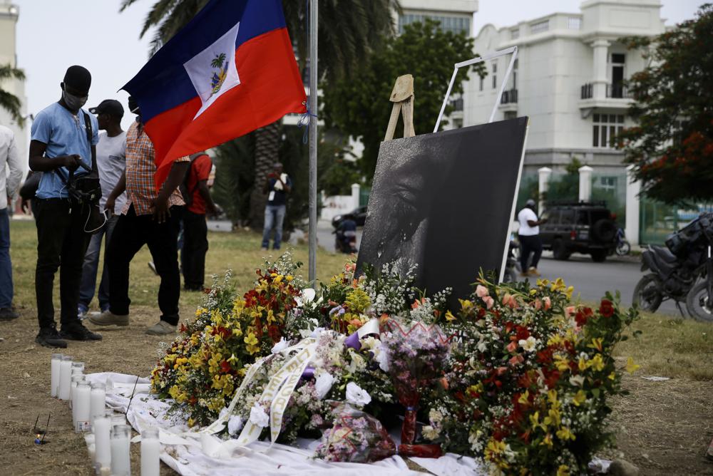 Una foto modificada para que el presidente Jovenel Moïse aparezca llorando, junto a una bandera nacional en un altar improvisado en memoria del mandatario asesinado ante el palacio presidencial, en Puerto Príncipe, Haití, el miércoles 14 de julio de 2021, una semana después de que Moïse fuera asesinado en su casa. (AP Foto/Joseph Odelyn)