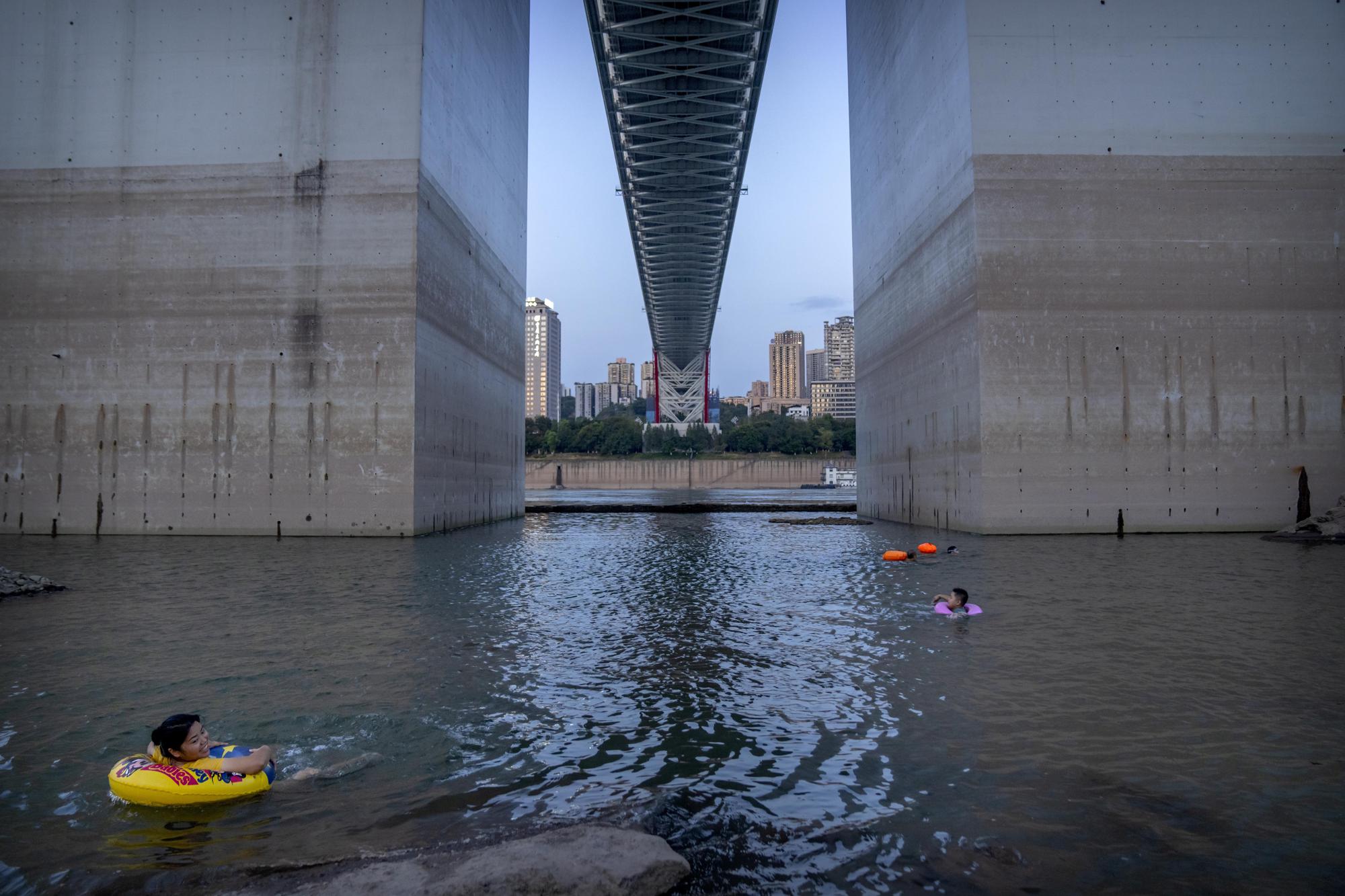 People float in the Yangtze River near bridge support columns that show previous water levels in southwestern China's Chongqing Municipality, Friday, Aug. 19, 2022. The very landscape of Chongqing, a megacity that also takes in surrounding farmland and steep and picturesque mountains, has been transformed by an unusually long and intense heat wave and an accompanying drought. (AP Photo/Mark Schiefelbein)