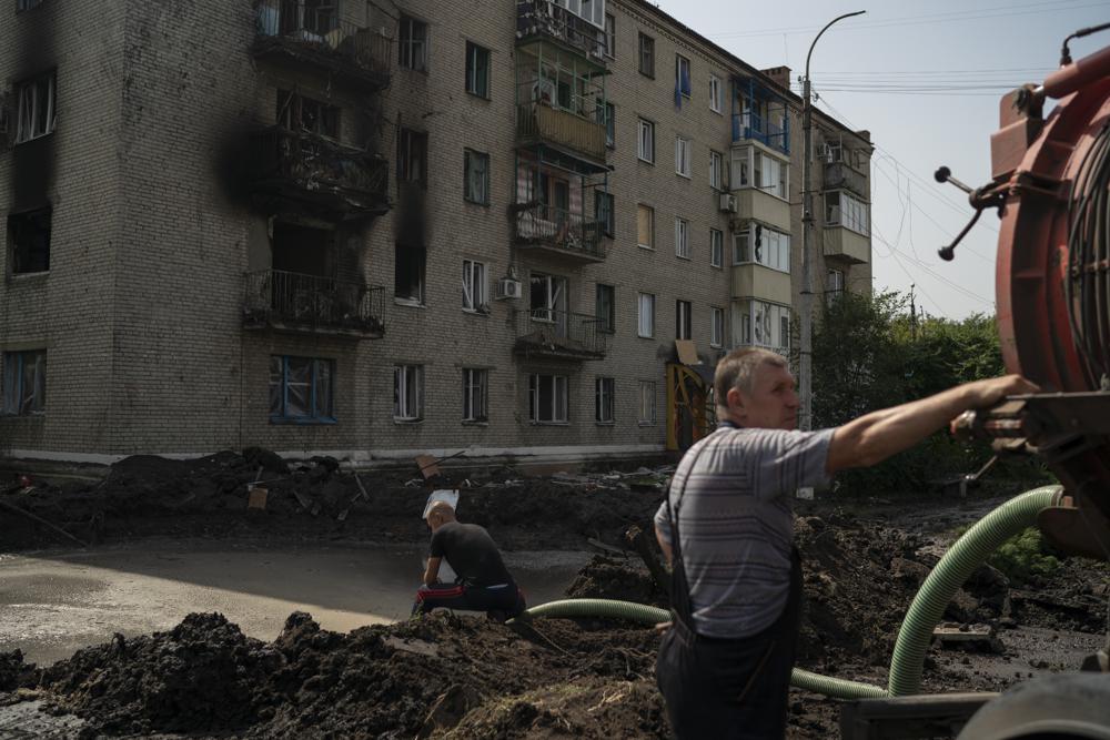 Workers drain water from a crater created by an explosion that damaged a residential building after a Russian attack in Slovyansk, Ukraine, Sunday, Aug. 28, 2022. (AP Photo/Leo Correa)