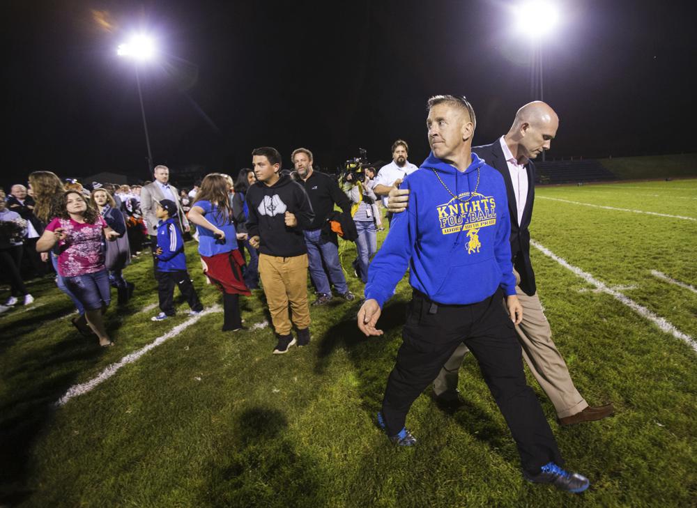 FILE - Bremerton High assistant football coach Joe Kennedy, front, walks off the field with his lawyer, right, Oct. 16, 2015, after praying at the 50-yard line following a football game in Bremerton, Wash. After losing his coaching job for refusing to stop kneeling in prayer with players and spectators on the field immediately after football games, Kennedy will take his arguments before the U.S. Supreme Court on Monday, April 25, 2022, saying the Bremerton School District violated his First Amendment rights by refusing to let him continue praying at midfield after games. (Lindsey Wasson/The Seattle Times via AP, File)