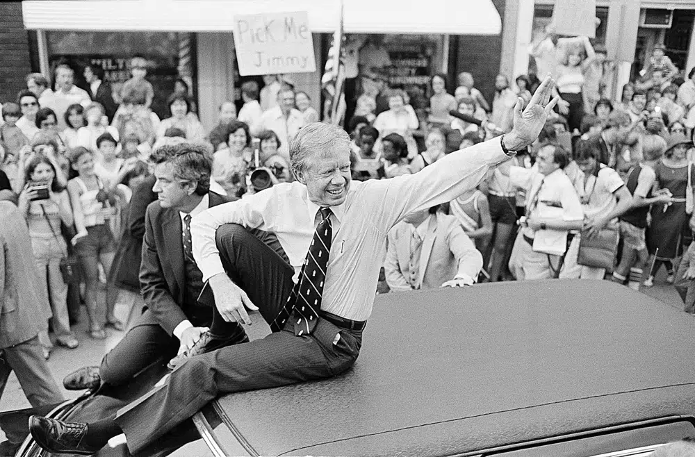 FILE - President Jimmy Carter waves from the roof of his car along the parade route through Bardstown, Ky., July 31, 1979. (AP Photo/Bob Daugherty, File)