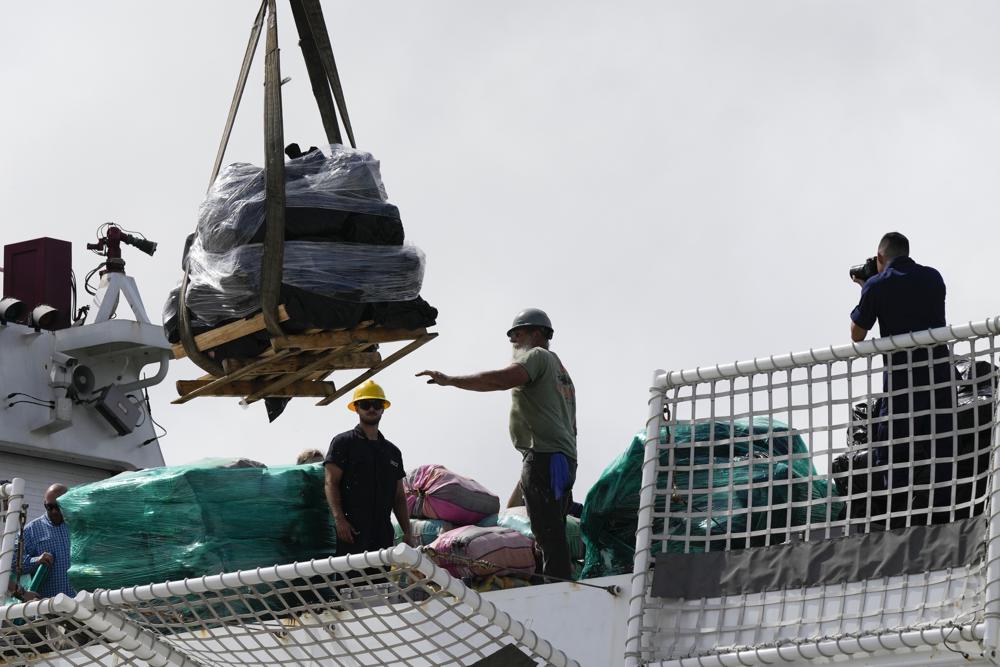 Los hombres sujetan paletas cargadas con paquetes de cocaína y marihuana incautados a una grúa, mientras la Guardia Costera de EE. UU. descarga más de mil millones de dólares en drogas incautadas del guardacostas Cutter James en Port Everglades, el jueves 17 de febrero de 2022, en Fort Lauderdale, Fla. La Guardia Costera dijo que el botín incluía aproximadamente 54,500 libras de cocaína y 15,800 libras de marihuana de múltiples interceptaciones en el Mar Caribe y el Pacífico oriental. (Foto AP/Rebecca Blackwell)