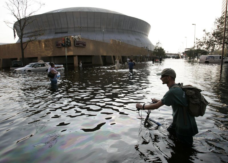 FILE - This Aug, 31, 2005, file photo shows a man pushing his bicycle through flood waters near the Superdome in New Orleans after Hurricane Katrina left much of the city under water. (AP Photo/Eric Gay, File)