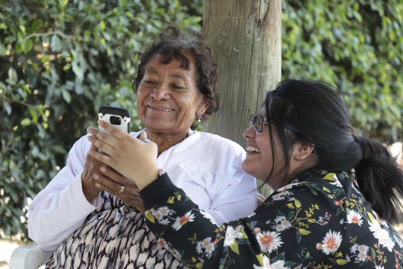 In this Dec. 23, 2016 photo, Tamara Alcala Dominguez shares cell phone photos with her grandmother Petra Bello Suarez in their home town of Molcaxac, Puebla, Mexico. During her first return since she left Mexico for the U.S. as a toddler, Alcala followed her grandmother everywhere, to the store, to meet neighbors and to the town holiday party. (AP Photo/Pablo Spencer)