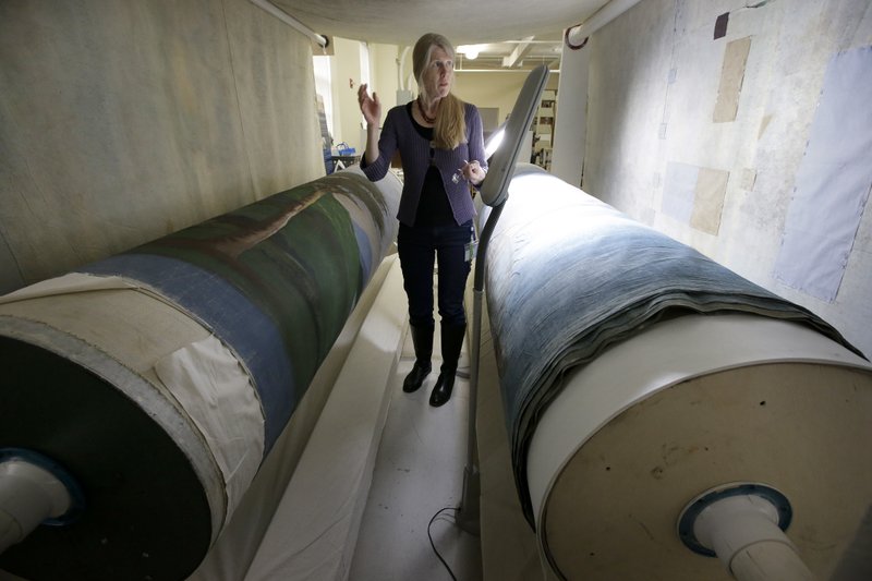 In this Tuesday, Nov. 7, 2017 photo textile conservator Kate Tarleton, of Rochester, Mass., stands between two oversized spools holding a portion of the 1848, "Grand Panorama of a Whaling Voyage Round the World," at the museum in New Bedford, Mass. The quarter-mile-long (0.4-kilometer-long) panorama toured the U.S. after it was completed in 1848. . (AP Photo/Steven Senne)