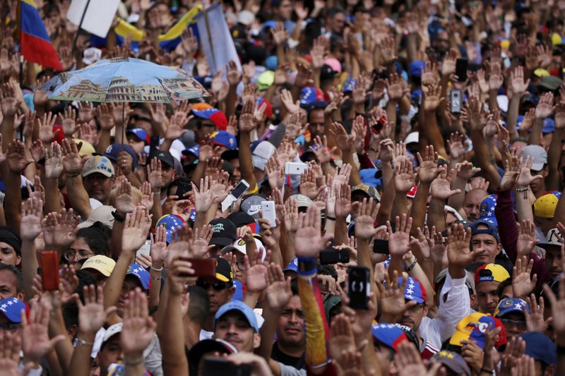 Anti-government protesters hold their hands up during the symbolic swearing-in of Juan Guaido, head of the opposition-run congress, who declared himself interim president of Venezuela. (AP Photo/Fernando Llano)