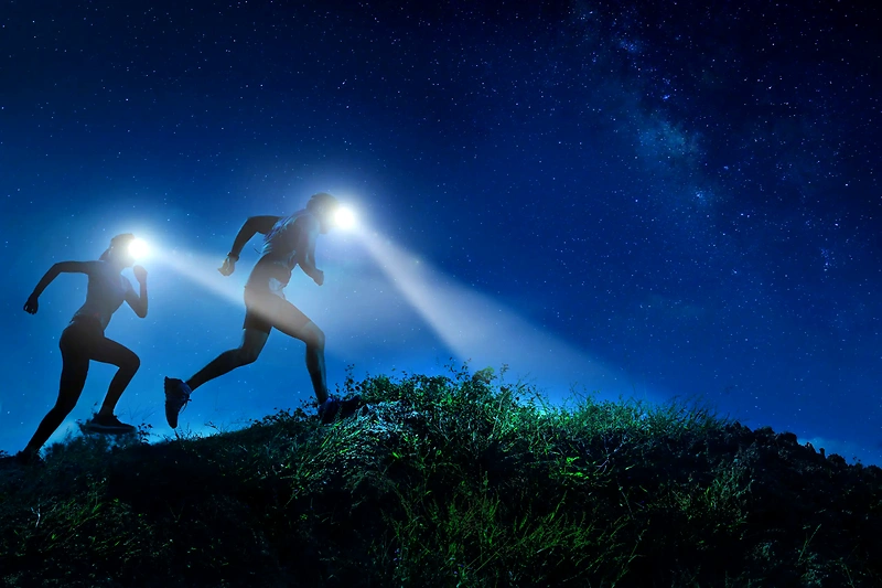 Twee lopers met koplampen rennen 's nachts een trail.