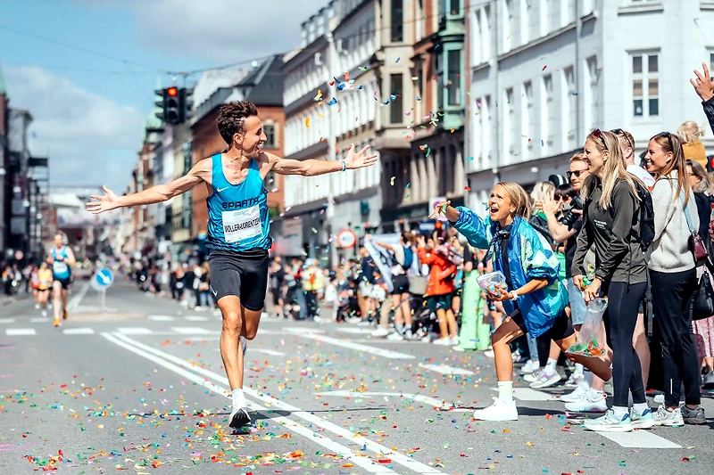 Maratonløber krydser målstregen, omgivet af jublende tilskuere og konfetti.