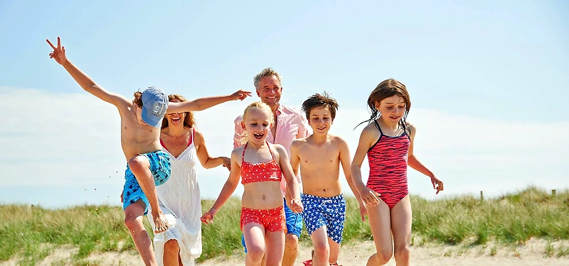 Glad familie løber på stranden. Perfekt til Familie Farveløbet!
