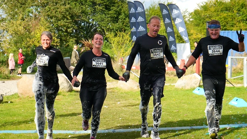 Fire glade deltagere i Mud Race Aarhus, dækket i mudder og skum.