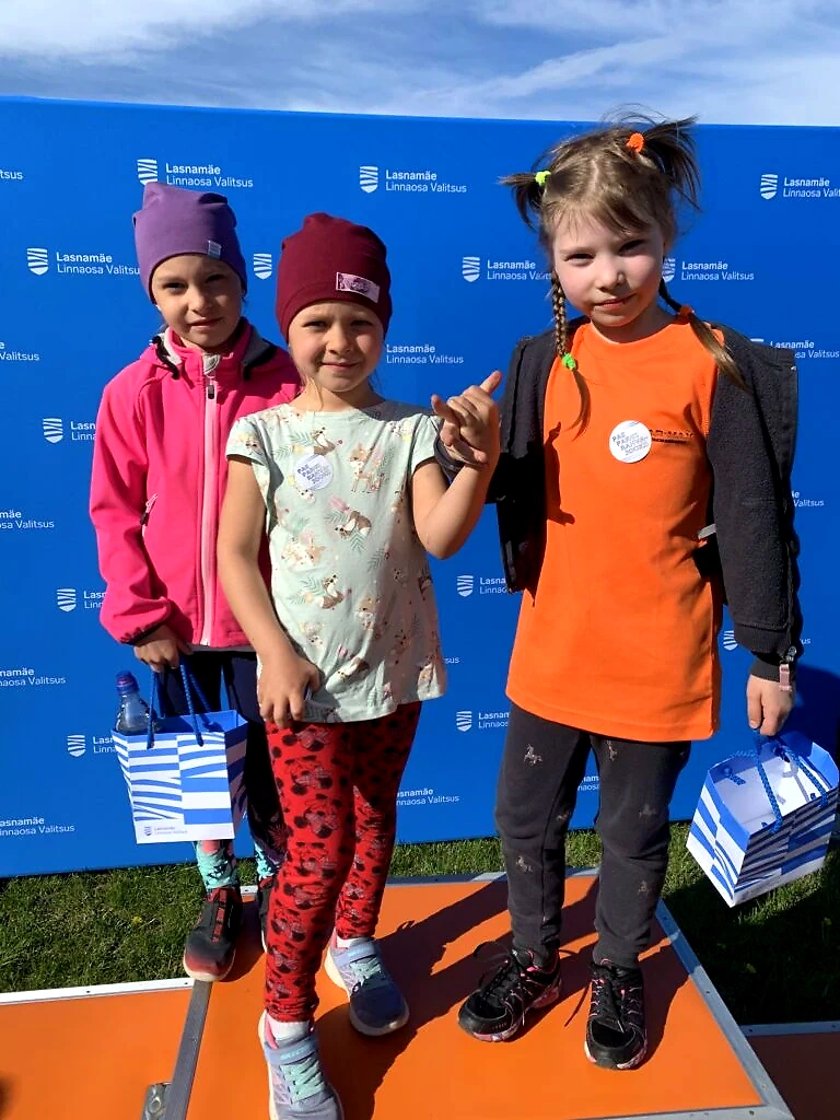 Children on the podium after the running event, against a backdrop of sponsor logos.