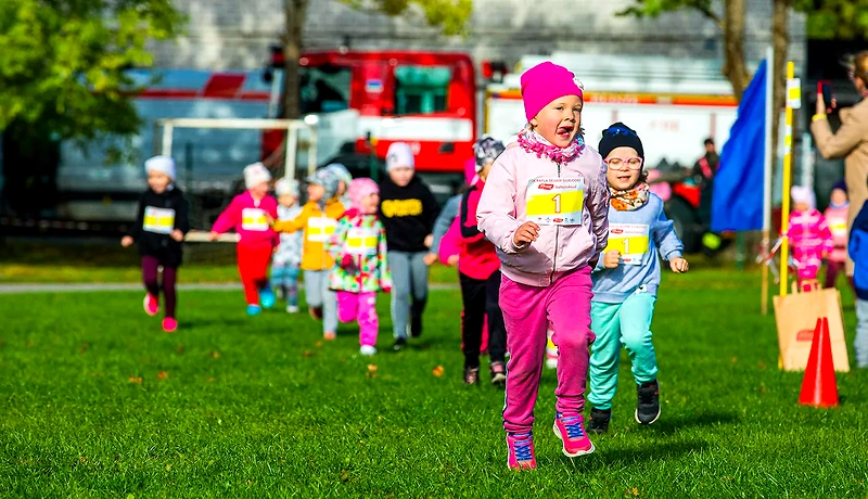 Children's race. Children in colorful outfits are running on the grass. The runners are facing the camera.