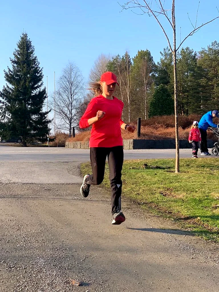 A runner in a red shirt is running outside on a trail.