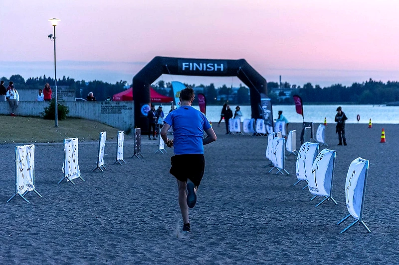 Juoksija lähestymässä maaliviivaa hiekkarannalla, jossa Helsinki Twilight Run järjestetään.