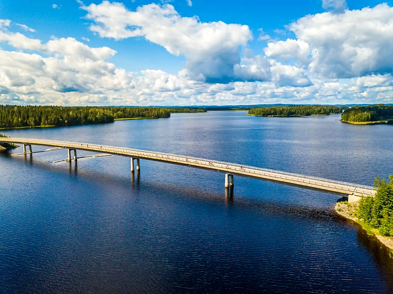 Maisemakuva sillalla juoksevista ihmisistä, vesistö ja metsä taustalla.