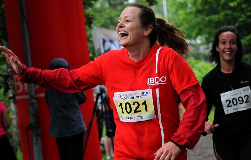 Runners in the BDO Mile Hamar. A woman in a red jacket is smiling broadly as she runs.
