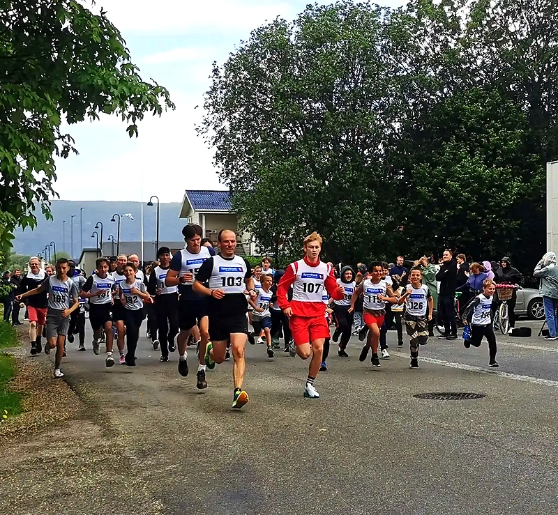 Participants are running in the Børløpet. Several children and adults are running on the paved road.