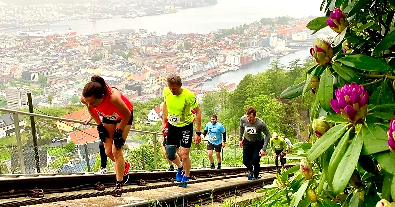 Runners in a steep uphill during a hill climb race, with a city in the background.