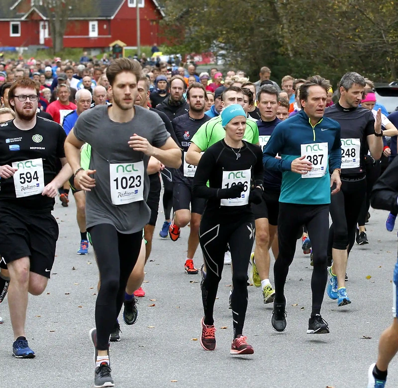 Runners in a race with bib numbers. Many people are running down a road.