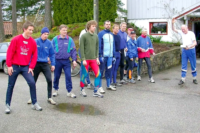 A group of runners gathered before or after the race. An older man waves.