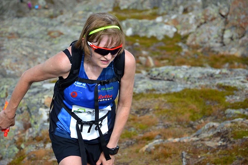 Runner in the Bystien Førde Opp, mountain running. The woman is in action in hilly terrain with a backpack and sunglasses.