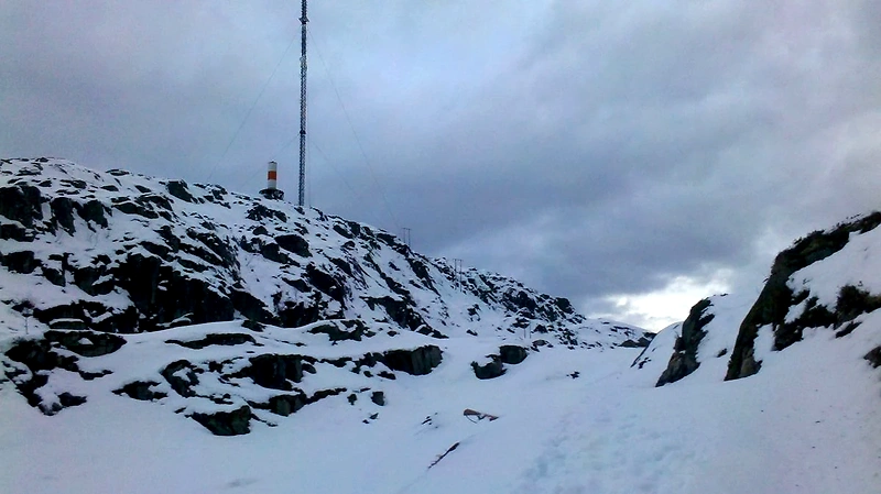 Snow-covered mountain landscape with a mountain peak and antenna, likely a hill climb race.