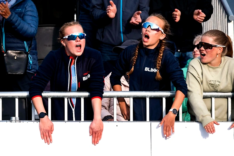 The crowd cheers at a race, with sunglasses and open mouths.