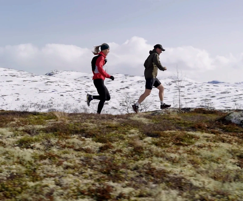 Runners on trails in a snowy mountain landscape.