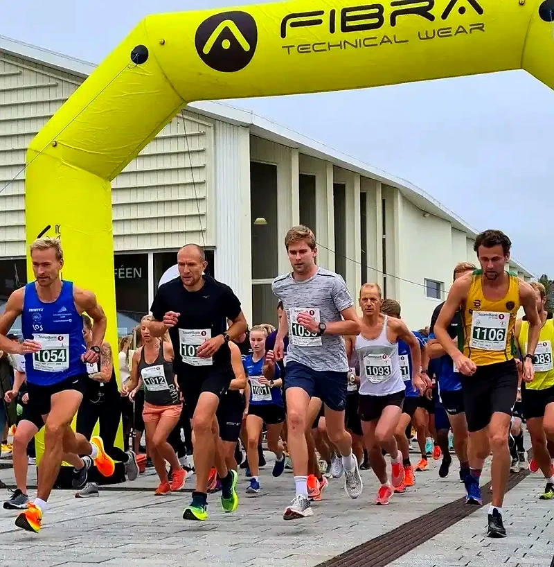 Runners who start a race under a yellow arch.