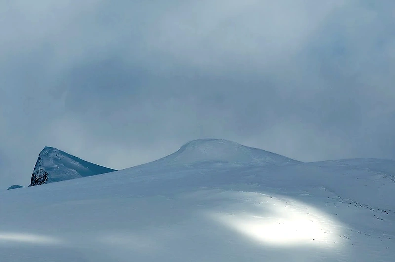 Snødekt fjellandskap under overskyet himmel.