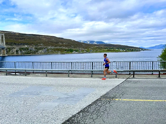 Runner on the bridge with the fjord and mountains in the background.