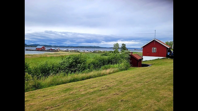 Utsikt over Jomfruland, med rød hus, grønt gress og hav. Perfekt for Jomfrulandsløpet.