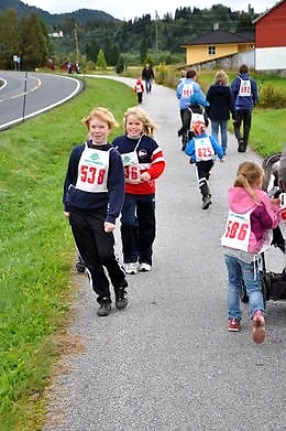 Children and adults are running in a race, with bib numbers on their chests.