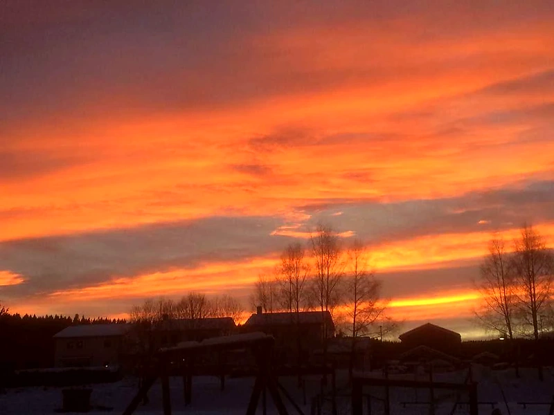 Sunset over a snow-covered landscape with buildings and trees.
