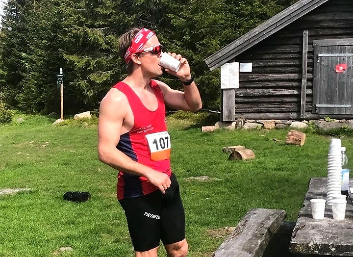 The runner drinks water after the race in nature.