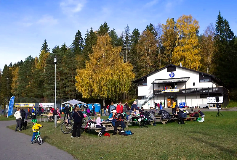People gathered at a running event, with a building in the background and children on bicycles.