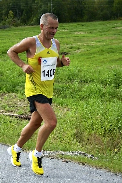 Runner in yellow and black running gear on asphalt road with bib number.