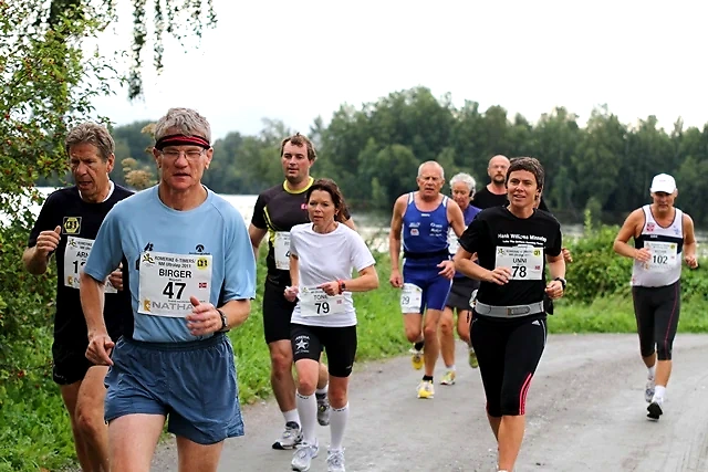 A group of people is running in a race. Several runners with bib numbers on a gravel road.