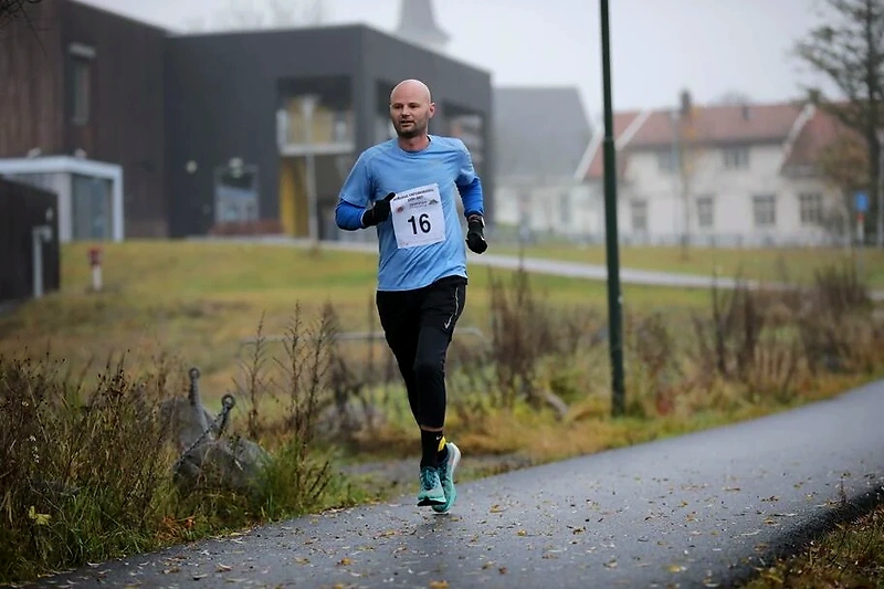 Runner in a race series with bib number 16 on a wet asphalt road.