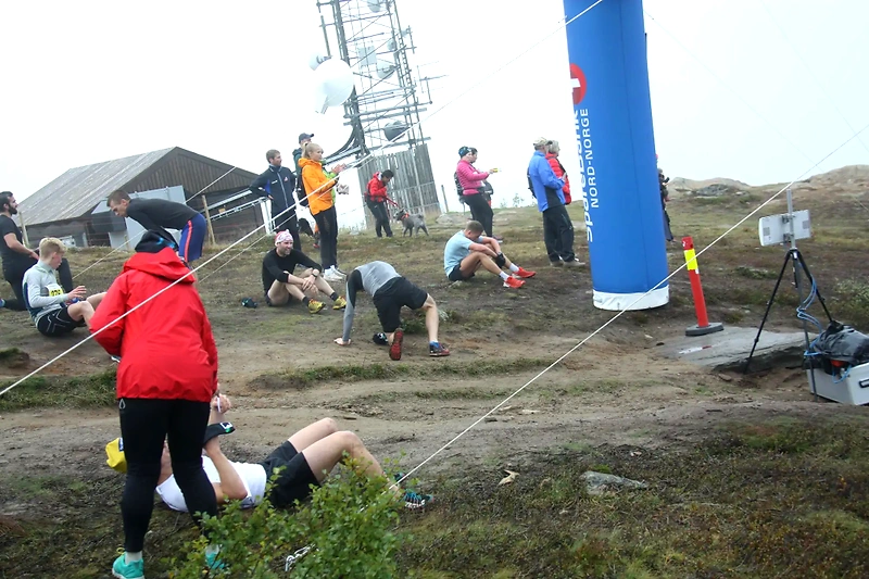 People at the top of a mountain peak with a finish line banner, possibly after a race.