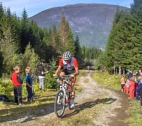 Cyclist on a gravel road with spectators in the terrain.